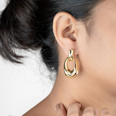 Gold hoop earring worn by a person with a neutral background